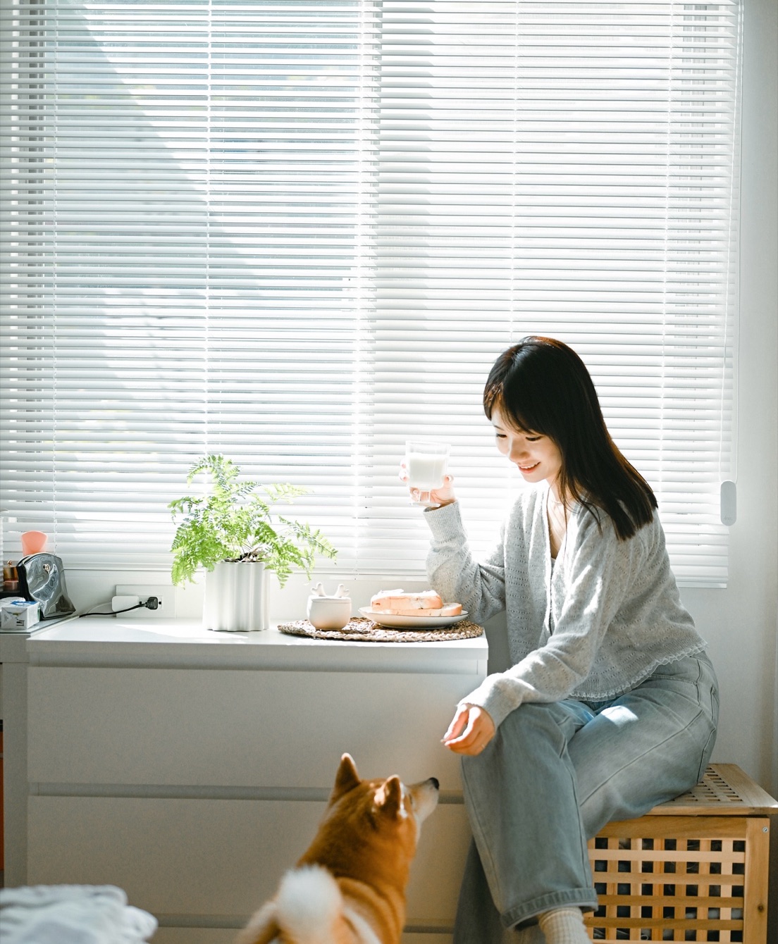 Mimi 坐在灑滿陽光的窗邊，和柴犬一起吃早餐